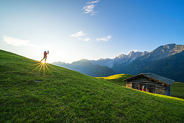 Man lit by the sunburst photographing Piz Badile and Cengalo, Tombal, Soglio, Val Bregaglia, canton of Graubunden, Switzerland, Europe