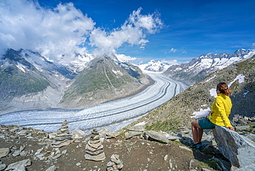 Side view of woman sitting on rocks admiring Aletsch Glacier from Eggishorn viewpoint, Bernese Alps, canton Valais, Switzerland, Europe