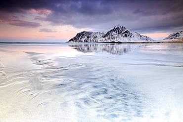 Sunset on Skagsanden beach surrounded by snow covered mountains reflected in the cold sea, Flakstad, Lofoten Islands, Arctic, Norway, Scandinavia, Europe