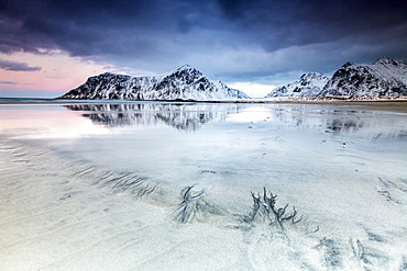 Sunset on Skagsanden beach surrounded by snow covered mountains reflected in the cold sea, Flakstad, Lofoten Islands, Arctic, Norway, Scandinavia, Europe