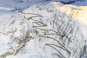 Narrow bends of the Stelvio Pass road on steep snowy mountain ridge, aerial view by drone, Bolzano province, South Tyrol side, Italy, Europe