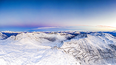 Pano by drone of sunrise over the narrow bends of Stelvio Pass mountain road covered with snow, Bormio, Valtellina, Lombardy, Italy, Europe