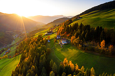 Sunbeam at sunset lighting the warm colors of autumn in Funes Valley, aerial view, Dolomites, Bolzano province, South Tyrol, Italy, Europe