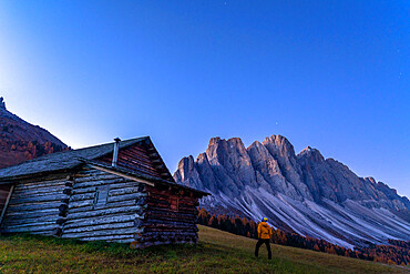 Man outside a hut admiring the Odle at sunrise, Gampen Alm, Funes Valley, Dolomites, Bolzano province, South Tyrol, Italy, Europe