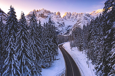 Aerial view by drone of car traveling on the scenic road Dobbiaco-Misurina along snowy woods at dawn, Dolomites, South Tyrol, Italy, Europe