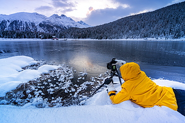 Photographer taking pictures of frozen Lej da Staz at dawn lying on the snow, Engadine, canton of Graubunden, Switzerland, Europe