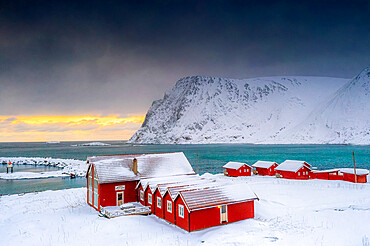 Winter sunset over the Arctic sea and fishermen cabins in the snow, Sorvaer, Soroya Island, Hasvik, Troms og Finnmark, Norway, Scandinavia, Europe