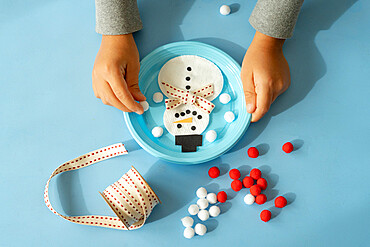 Hands of child creating a snowman with ribbon and pompom at Christmas time, Italy, Europe