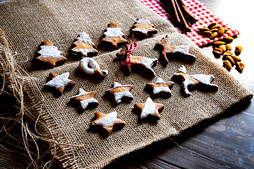 Gingerbread and butter cookies in shape of Christmas tree, stars and reindeer on canvas place mat on wood table background, Italy, Europe