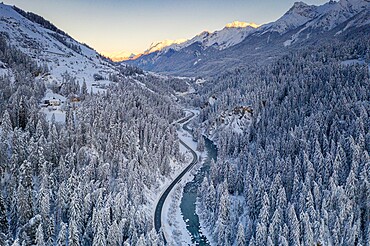 Sunrise over winding mountain road and frozen river in the forest covered with snow, Zernez, Graubunden Canton, Switzerland, Europe