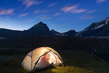 Silhouette of hiker inside the illuminated tent above lake Limmernsee at dusk, Canton of Glarus, Switzerland, Europe