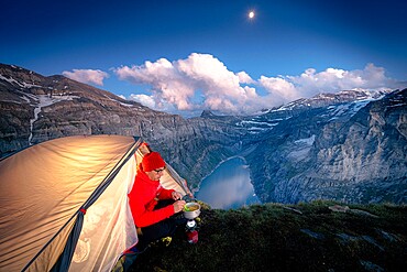 Hiker man with tent using camping stove on ridge above lake Limmernsee, Canton of Glarus, Switzerland, Europe