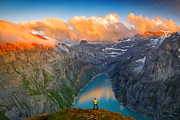 Man standing on rocks looking at clouds at sunset over lake Limmernsee, aerial view, Canton of Glarus, Switzerland, Europe