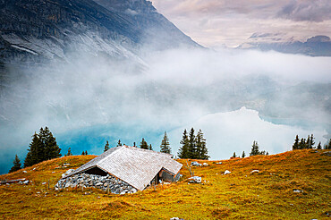 Hut on mountain ridge above lake Oeschinensee covered by mist, Bernese Oberland, Kandersteg, canton of Bern, Switzerland, Europe