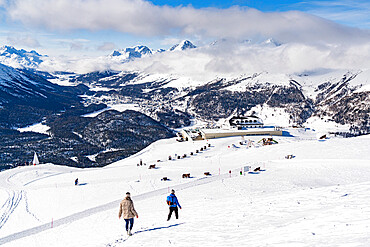 Two hikers walking on snowy slope towards the funicular station at Muottas Muragl, Samedan, Engadine, Graubunden, Switzerland, Europe