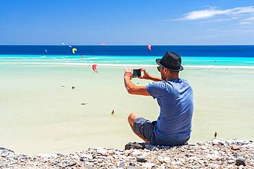 Tourist with straw hat photographing kiteboarders with smartphone at Sotavento beach, Jandia, Fuerteventura, Canary Islands, Spain, Atlantic, Europe