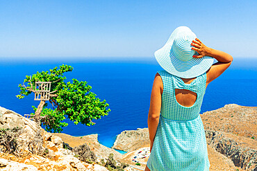 Back view of young woman with dress and sun hat watching the sea, Crete, Greek Islands, Greece, Europe