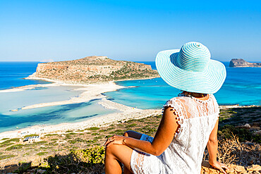 Portrait of woman with hat admiring the idyllic beach and lagoon sitting on top of hill, Balos, Crete, Greek Islands, Greece, Europe