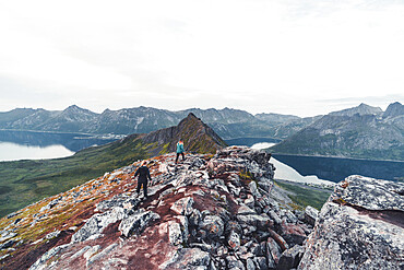 Two young women hikers climbing the rocks on Hesten Mountain peak, Senja, Troms county, Norway, Scandinavia, Europe