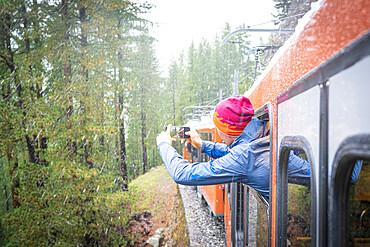 Man photographing the snow falling over the forest leaning out of Gornergrat Bahn train, Zermatt, Valais canton, Switzerland, Europe