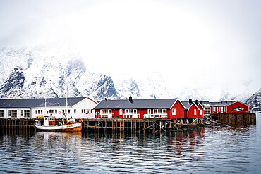 Foggy sky over snowcapped mountains and traditional Rorbu cabins by the sea, Hamnoy, Nordland county, Lofoten Islands, Norway, Scandinavia, Europe