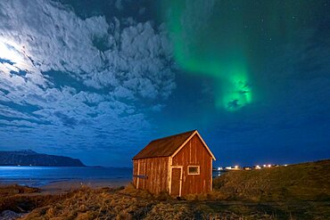 Red cabin under the bright night sky lit by moon and Northern Lights, Ramberg, Nordland county, Lofoten Islands, Norway