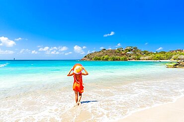 Beautiful woman with orange dress and straw hat standing on a tropical beach, Antigua, Caribbean, West Indies