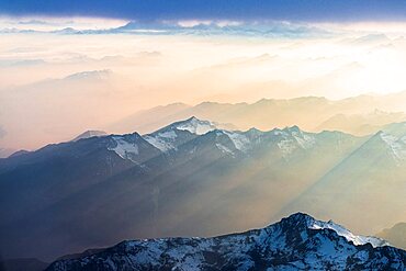 Flying over the snowcapped peaks of Lepontine and Ticino Alps lit by sun rays in the romantic sky at sunset, Switzerland