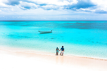 Man and woman holding hands on a tropical beach admiring the crystal clear sea, aerial view, Antigua and Barbuda, West Indies, Caribbean, Central America