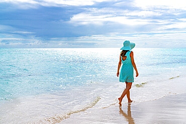 Woman walking on a white sand beach under the cloudy sky at sunset, Barbuda, Antigua and Barbuda, West Indies, Caribbean, Central America