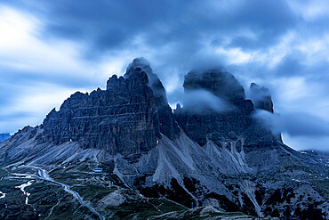 Clouds at dusk in the foggy sky over Tre Cime di Lavaredo mountain peaks, Dolomites, South Tyrol, Italy, Europe