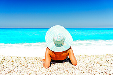 Carefree woman with straw hat sunbathing lying on a idyllic beach, Kefalonia, Ionian Islands, Greek Islands, Greece, Europe