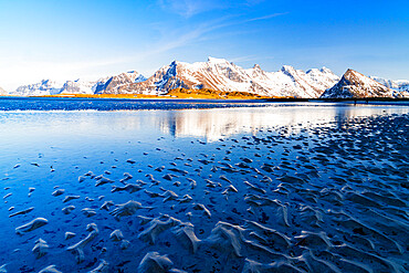 Waves of the cold sea crashing on the beach with snowy mountains on background, Fredvang, Nordland, Lofoten Islands, Norway, Europe