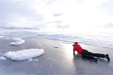 Man photographing the snowy landscape lying down on a frozen lake, Stora Sjofallet, Norrbotten County, Lapland, Sweden, Scandinavia, Europe