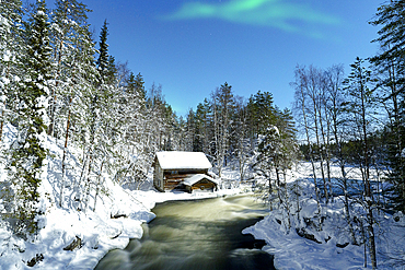 Aurora Borealis (Northern Lights) over a chalet overlooking Myllikoski rapids of frozen river, Ruka Kuusamo, Lapland, Finland, Europe