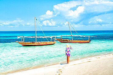 Cheerful woman with hat admiring the crystal clear sea standing on a beach, Kwale Island, Zanzibar, Tanzania