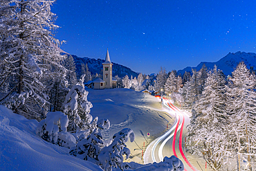 Car trails lights on snowy mountain road leading to Chiesa Bianca under the stars, Maloja, Graubunden, Engadin, Switzerland