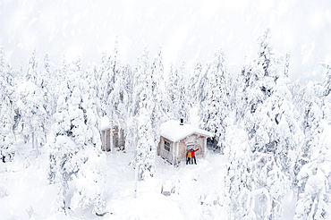 Aerial view of happy couple enjoying the winter holidays in a frozen hut in the snowy forest, Iso Syote, Northern Ostrobothnia, Lapland, Finland