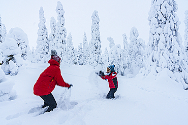 Cheerful mother and son enjoying playing with snow in the winter landscape of Finnish Lapland, Finland, Europe