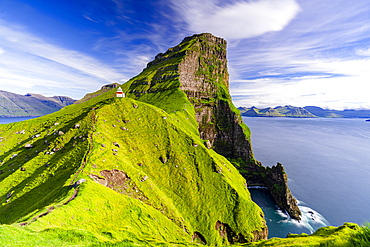 Kallur lighthouse on cliffs covered with grass with Borgarin mountain peak on background, Kalsoy island, Faroe Islands, Denmark, Europe