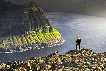 One man admiring the majestic cliffs along a fjord standing on top of mountain during a hike, Vidoy Island, Faroe Islands, Denmark, Europe