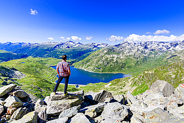 One man looking at the alpine lake of Montespluga standing on rocks, Madesimo, Valle Spluga, Valtellina, Lombardy, Italy, Europe