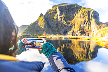 Personal perspective of woman photographing mountains in autumn with smartphone, A i Lofoten, Moskenes, Lofoten Islands, Nordland, Norway, Scandinavia, Europe