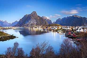 Dusk over majestic Olstind mountain overlooking the iconic harbor of the fishing village of Reine, Lofoten Islands, Nordland, Norway, Scandinavia, Europe