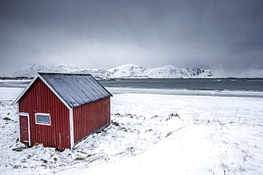 A typical house of the fishermen called rorbu on the snowy beach frames the icy sea at Ramberg, Lofoten Islands, Arctic, Norway, Scandinavia, Europe