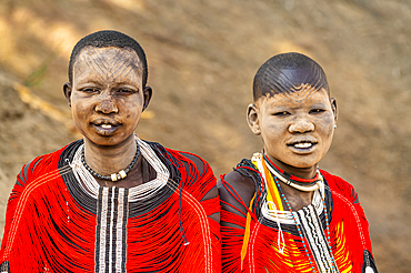 Mundari women in traditional dresses with facial scarring and ash on faces, posing on a rock, Mundari tribe, South Sudan, Africa