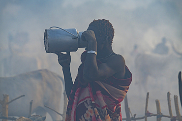 Backlight photo of a man in a Mundari cattle camp drinking milk, Mundari tribe, South Sudan, Africa