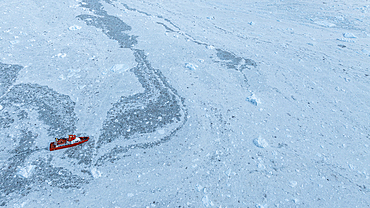 Aerial of a little ship floating between the ice below the Eqi glacier, Western Greenland