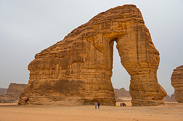 Locals standing in the giant arch of Elephant Rock, Al Ula, Saudi Arabia, Middle East