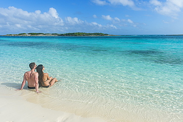 Couple sitting on a white sand beach in the turquoise waters of the Exumas, Bahamas, West Indies, Caribbean, Central America